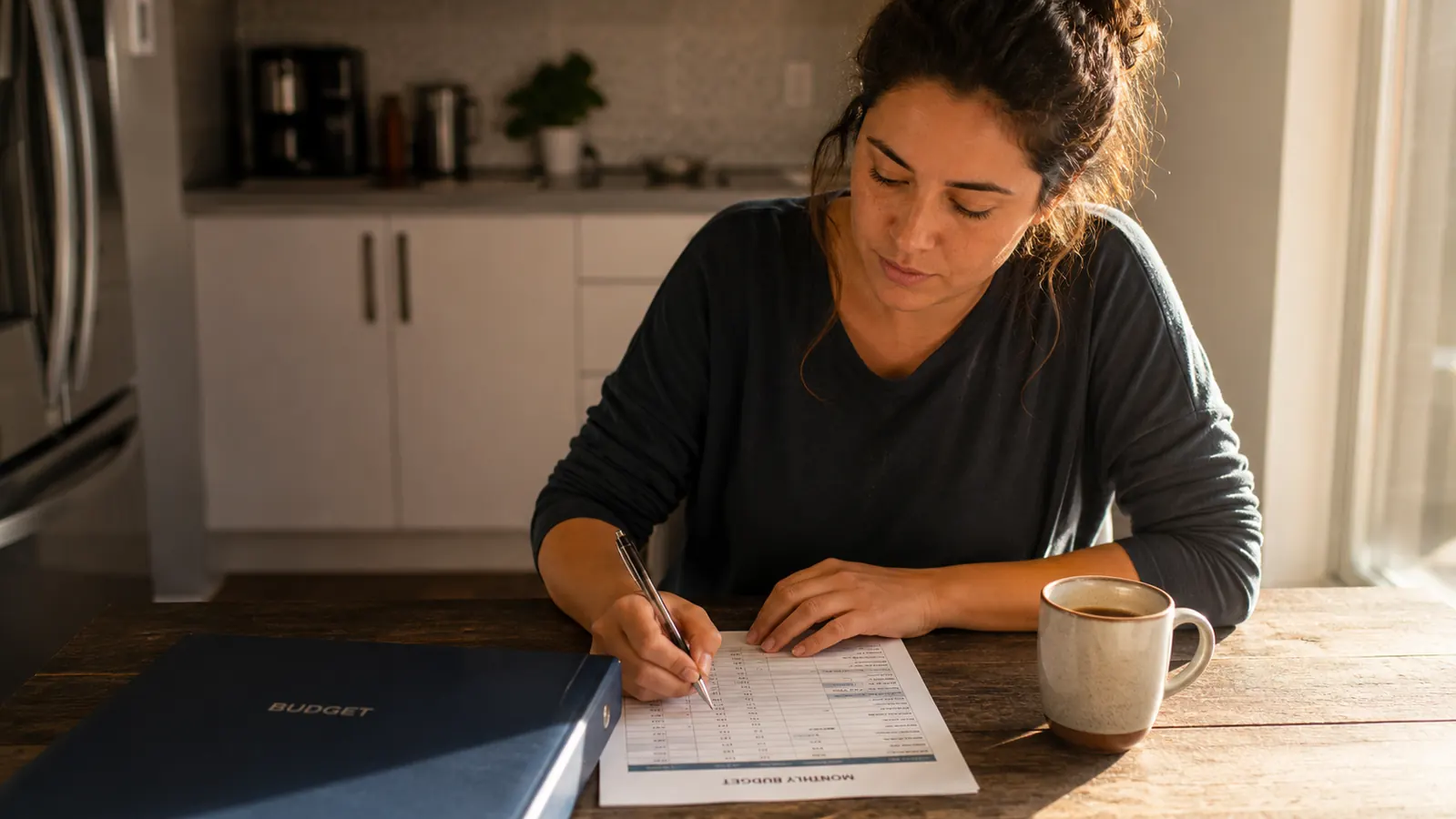 Woman smiling while writing in a budget worksheet, SKYDUE binder open in front of her