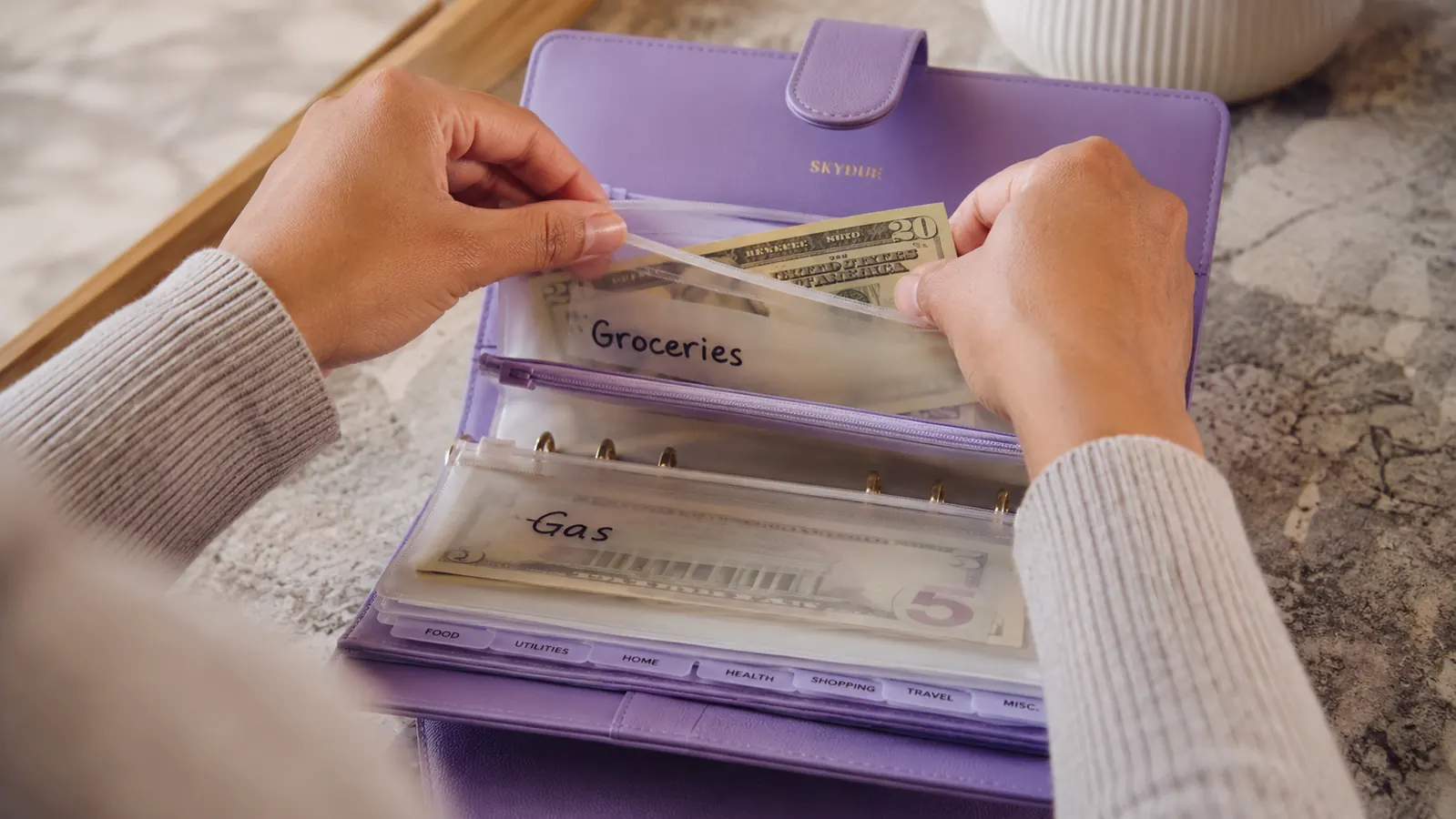 Hands sorting cash bills into labeled envelope categories inside an open budget binder